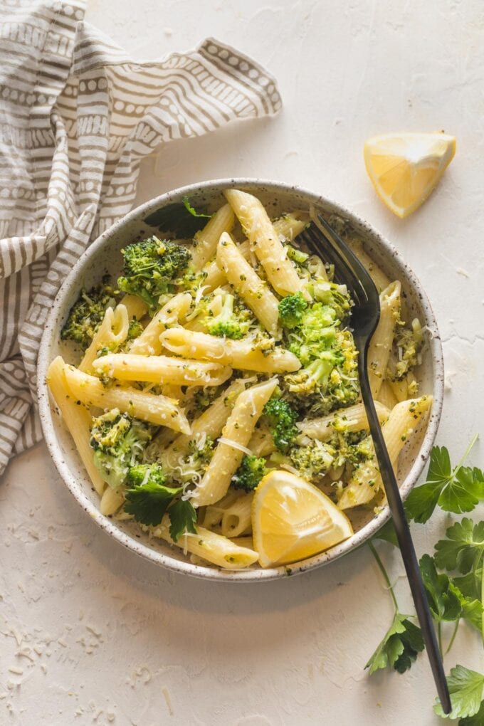 Small bowl of lemon broccoli pasta served with Parmesan and an extra lemon wedge.