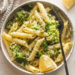 Small bowl of lemon broccoli pasta served with Parmesan and an extra lemon wedge.