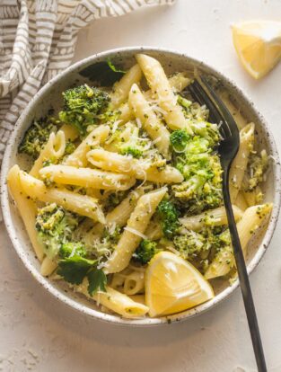 Small bowl of lemon broccoli pasta served with Parmesan and an extra lemon wedge.