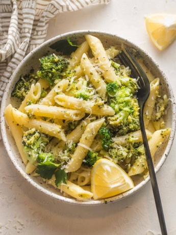 Small bowl of lemon broccoli pasta served with Parmesan and an extra lemon wedge.