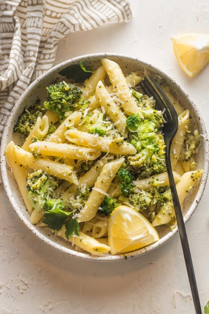 Small bowl of lemon broccoli pasta served with Parmesan and an extra lemon wedge.