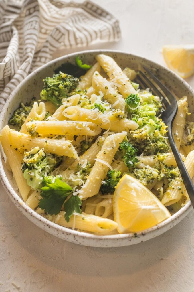 Small bowl of lemon broccoli pasta served with Parmesan and an extra lemon wedge.