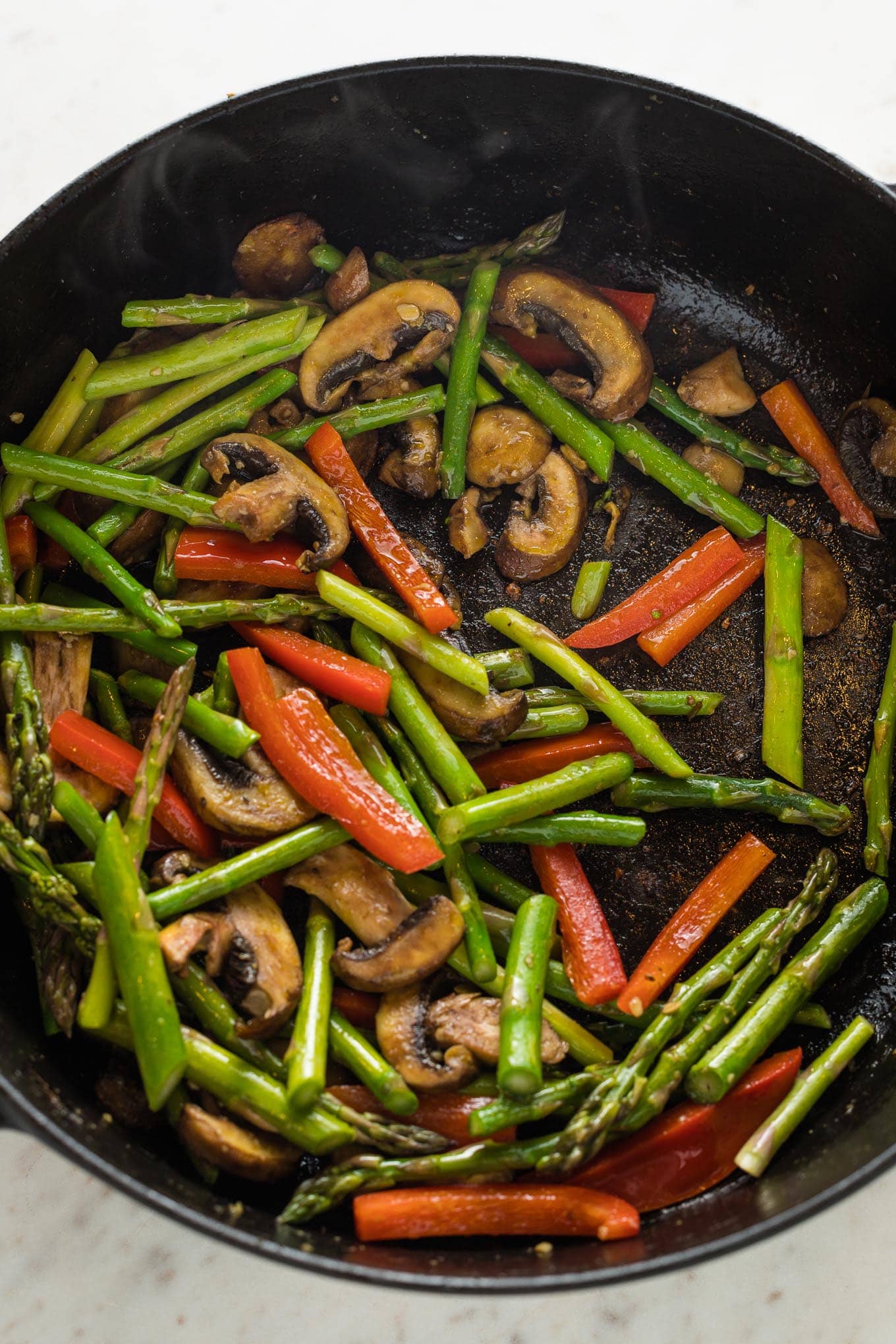 Tender crisp asparagus, red bell pepper, and sliced mushrooms cooked in a skillet.