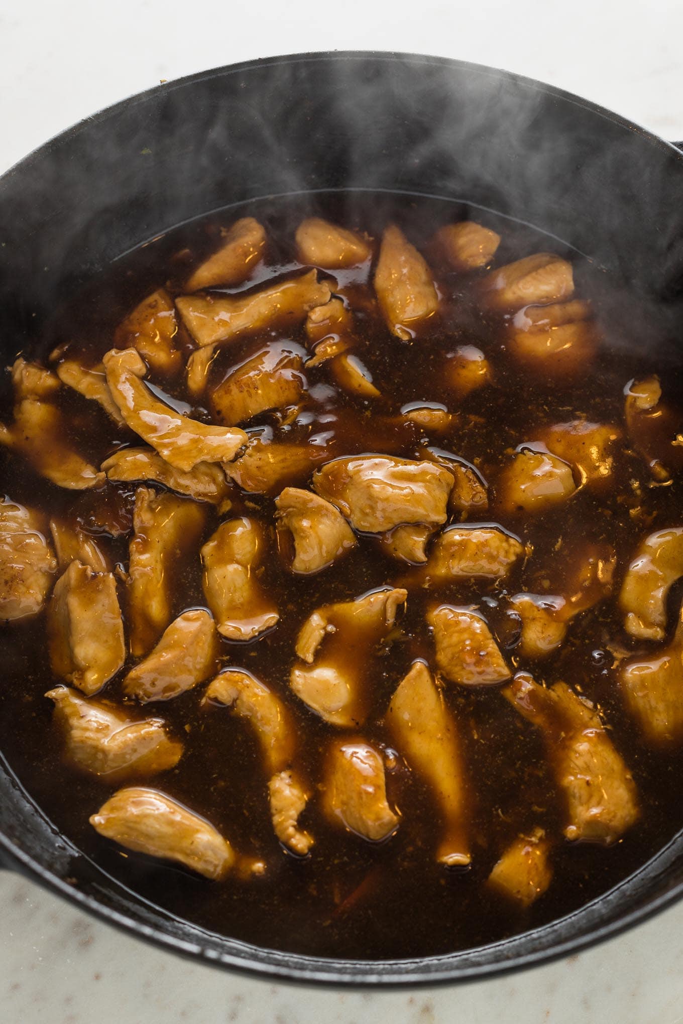 Stir fry sauce coating thinly-sliced chicken in a large skillet.