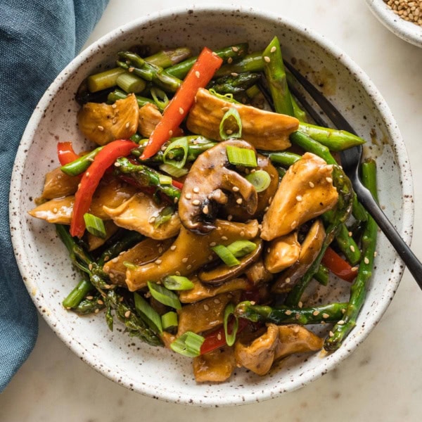 White bowl with a serving of chicken asparagus stir fry ready to eat.