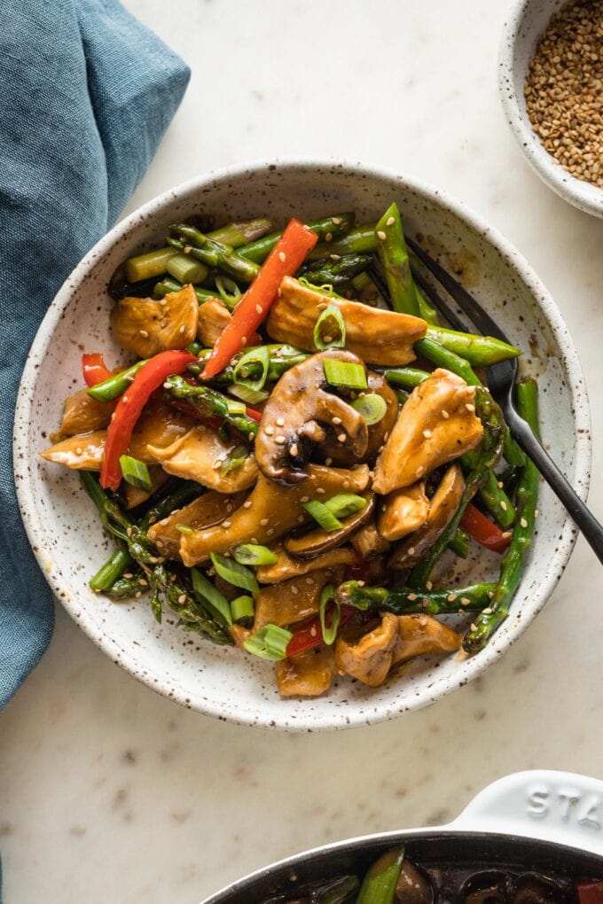 White bowl with a serving of chicken asparagus stir fry ready to eat.