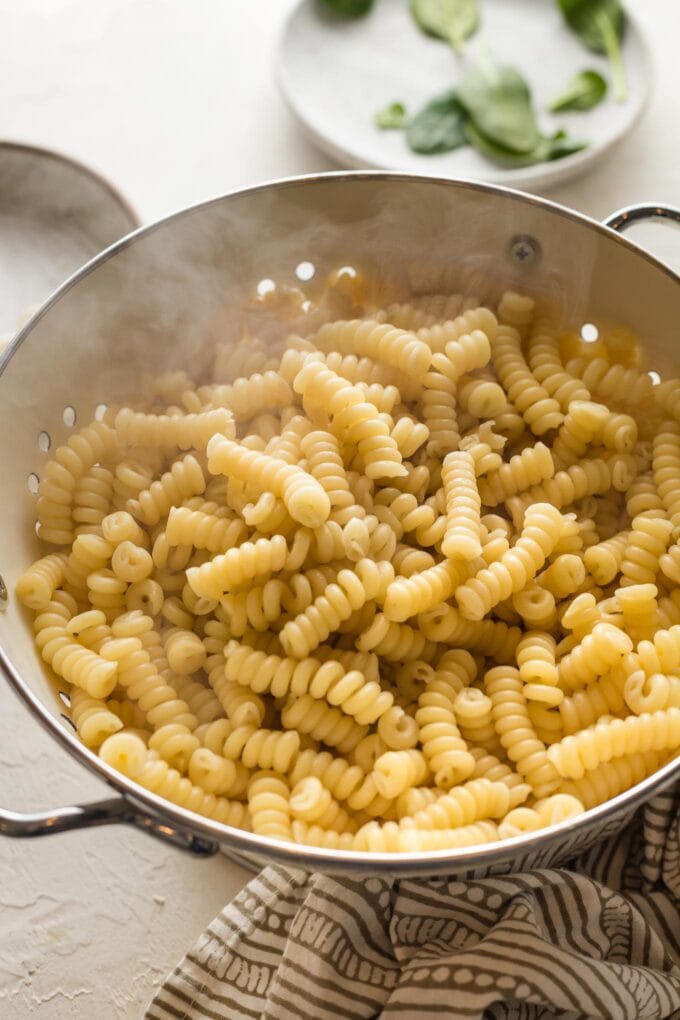 Just-cooked bucati pasta cooling in a colander.