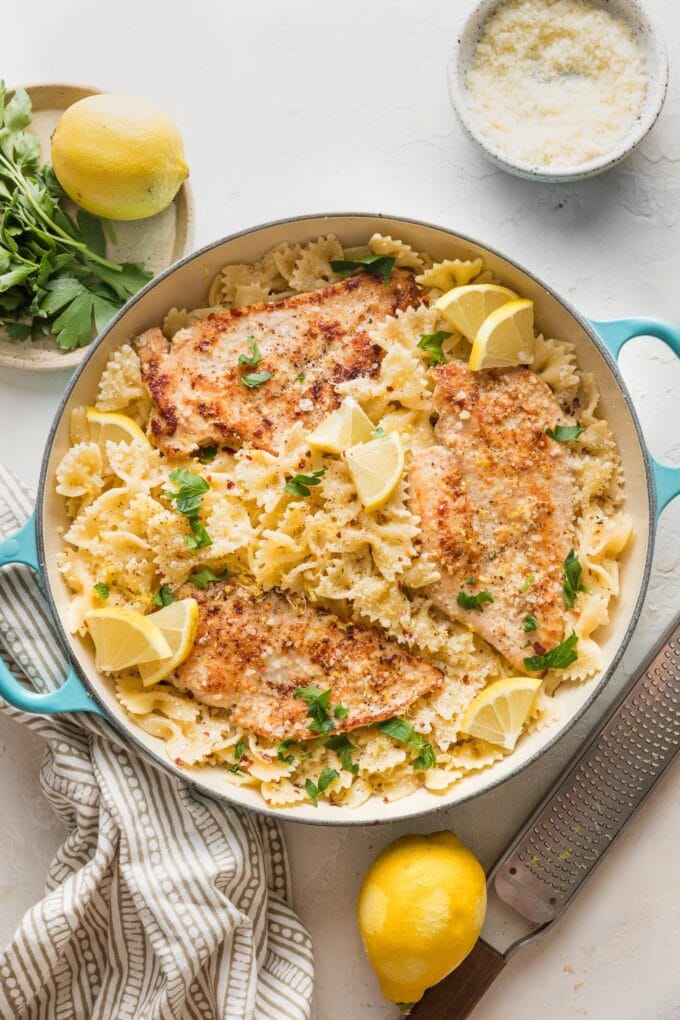 Finished skillet of lemon chicken pasta garnished with lemon wedges, parsley, and extra Parmesan cheese.