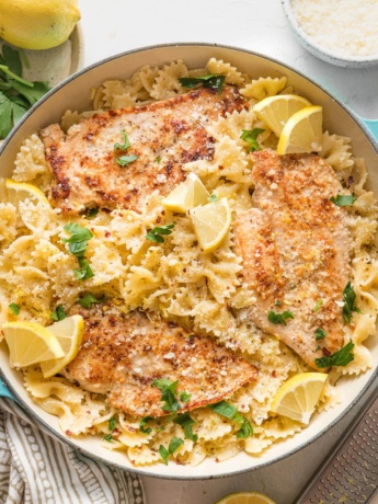 Skillet full of lemon chicken pasta in a light citrus sauce, garnished with lemon wedges and fresh Italian parsley.