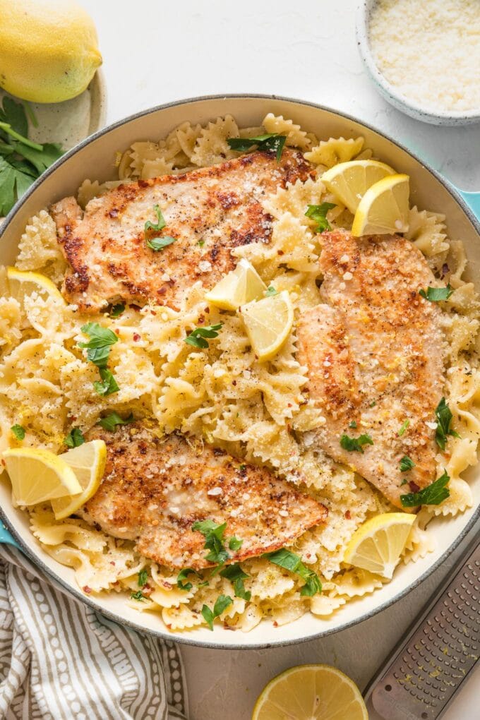 Skillet full of lemon chicken pasta in a light citrus sauce, garnished with lemon wedges and fresh Italian parsley.