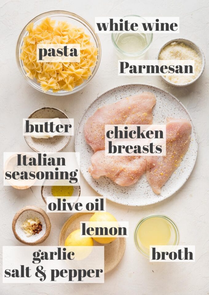 Labeled overhead image of dried farfalle pasta, chicken breasts, white wine, grated Parmesan cheese, butter, olive oil, Italian seasoning, minced garlic, salt, black pepper, broth, and a lemon, all in prep bowls and ready to measure and cook.