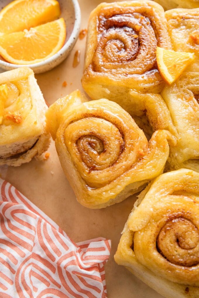 A fluffy orange cinnamon roll with gooey glaze and extra orange wedges scattered nearby for garnish.