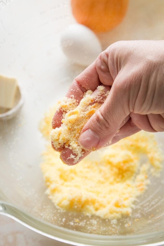 Close up image of someone using their fingers to rub orange zest into granulated sugar.