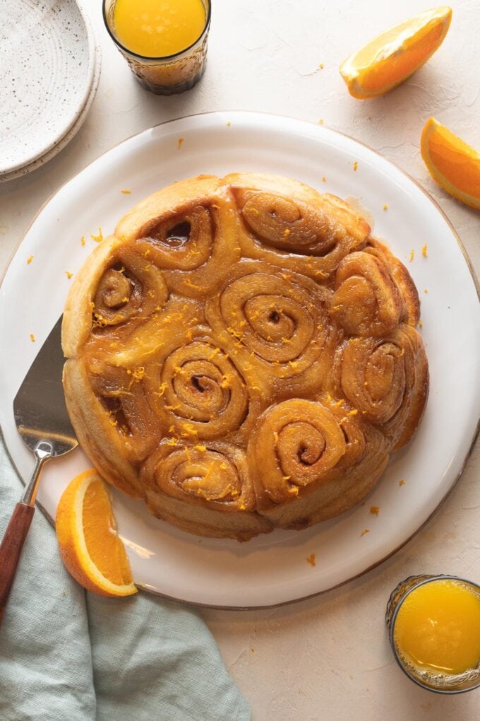 Orange sweet rolls turned upside down onto a serving plate, served with fresh orange slices and orange juice.