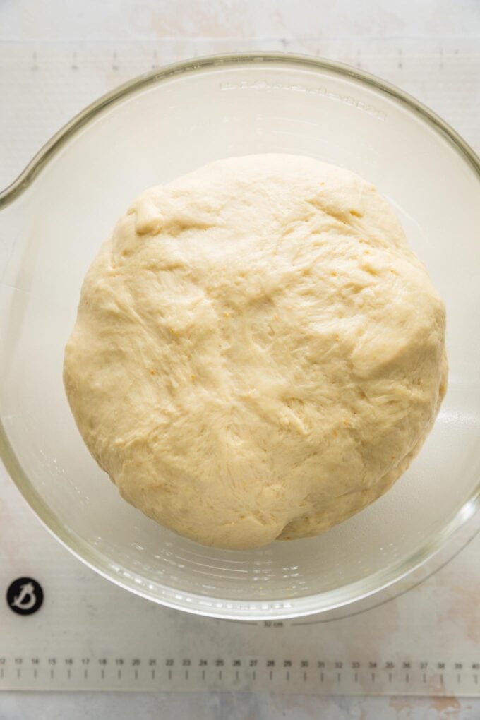 Dough for cinnamon orange rolls puffy and risen to about double its original size in a clear glass stand mixer bowl.