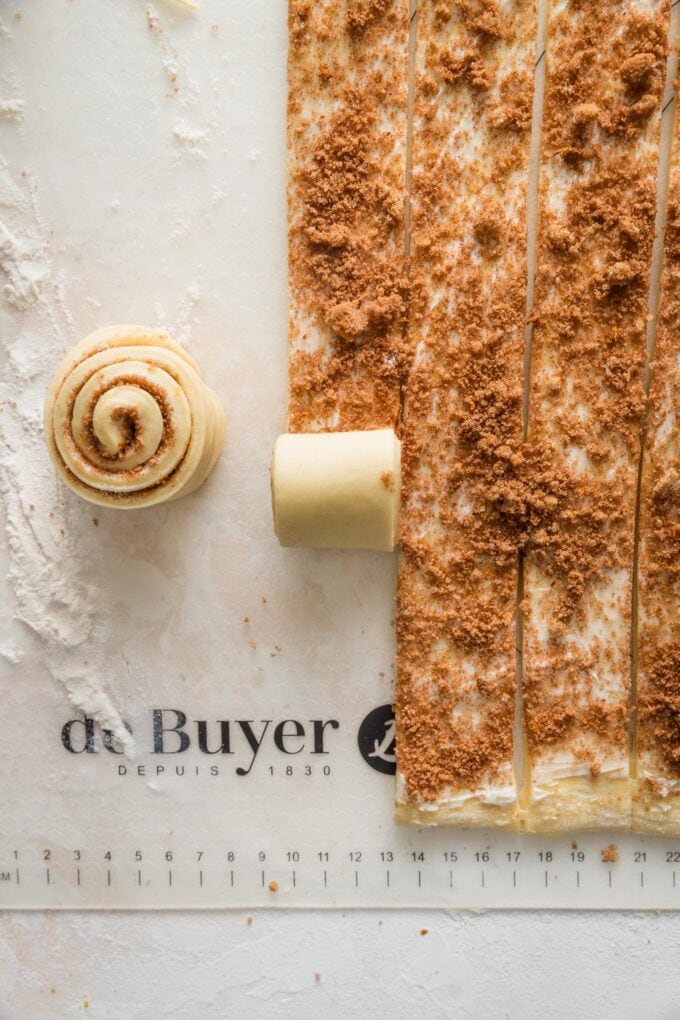 Process shot of orange sweet roll dough being rolled up into rolls ready to bake.