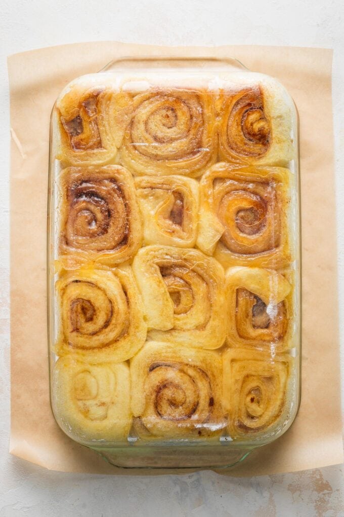 Clear glass baking pan full of orange sweet rolls, turned upside down on top of a piece of parchment paper.