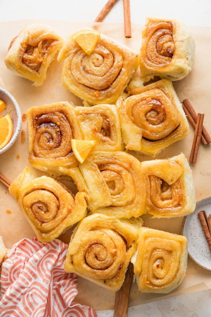 Batch of 12 glazed orange sweet rolls spread out on a counter and sprinkled with extra fresh orange zest.