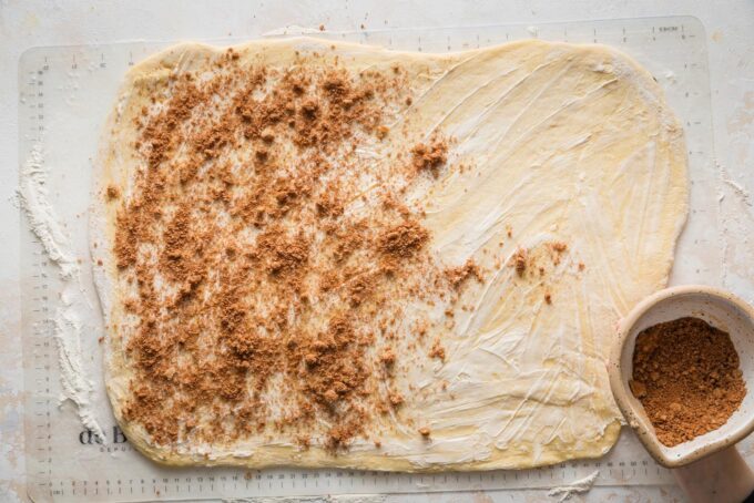 Orange cinnamon roll dough rolled out into a large rectangle, coated with softened butter, and partially sprinkled with a mixture of cinnamon, brown sugar, and orange zest.