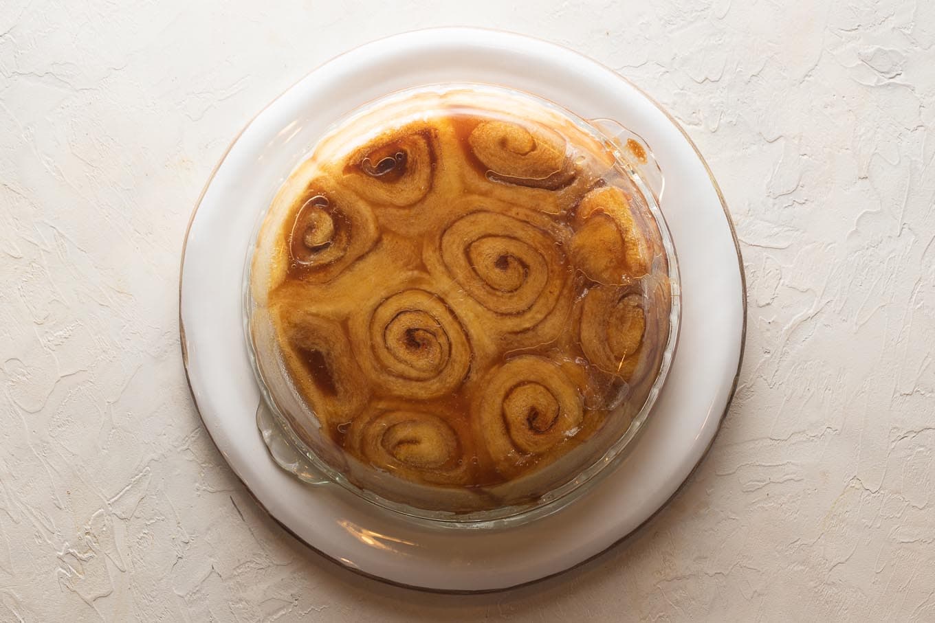 Pie plate turned over upside-down on top of a serving plate, so the rolls fall out and the glaze falls out on top of them.