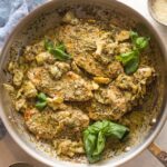 Skillet filled with creamy pesto artichoke chicken served with Parmesan and fresh basil leaves.
