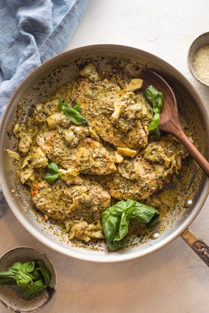 Skillet with pesto artichoke chicken and a wooden spoon about to serve portions.