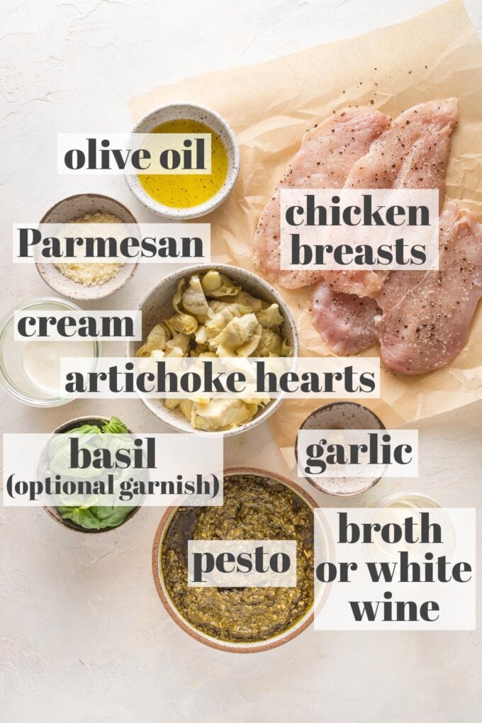 Labeled photo of prep bowls and parchment holding chicken breasts, olive oil, Parmesan, cream, artichoke hearts, fresh basil, pesto, garlic, and white wine, which can be substituted with chicken broth.