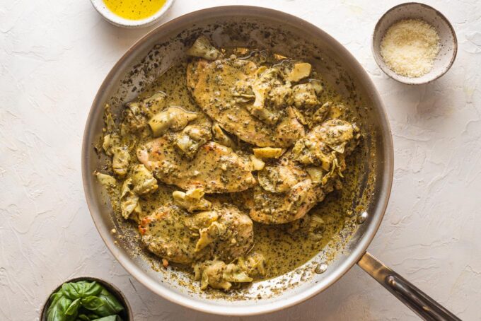 Chicken breasts returned to the skillet with pesto cream sauce and artichokes spooned on top.