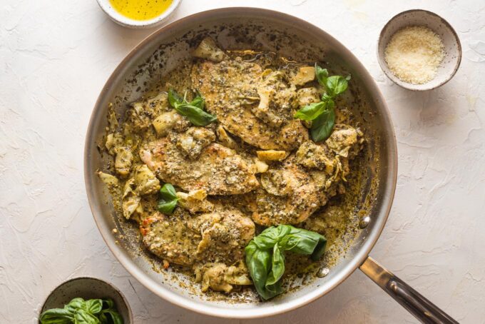 Pesto artichoke chicken skillet garnished with fresh basil and grated Parmesan cheese.
