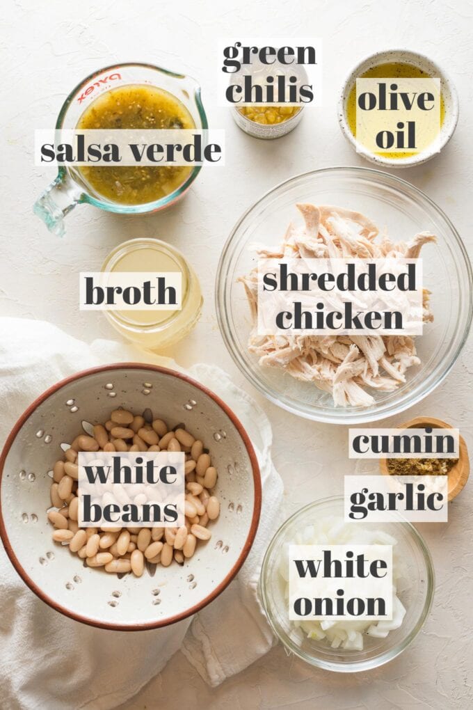 Labeled photo showing prep bowls filled with salsa verde, shredded chicken, white beans, white onion, garlic, cumin, chicken broth, green chiles, and olive oil.