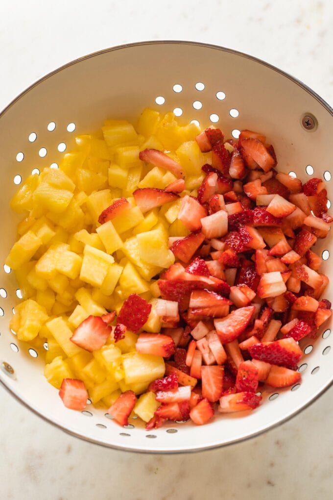 Diced strawberries and pineapple together in a colander.