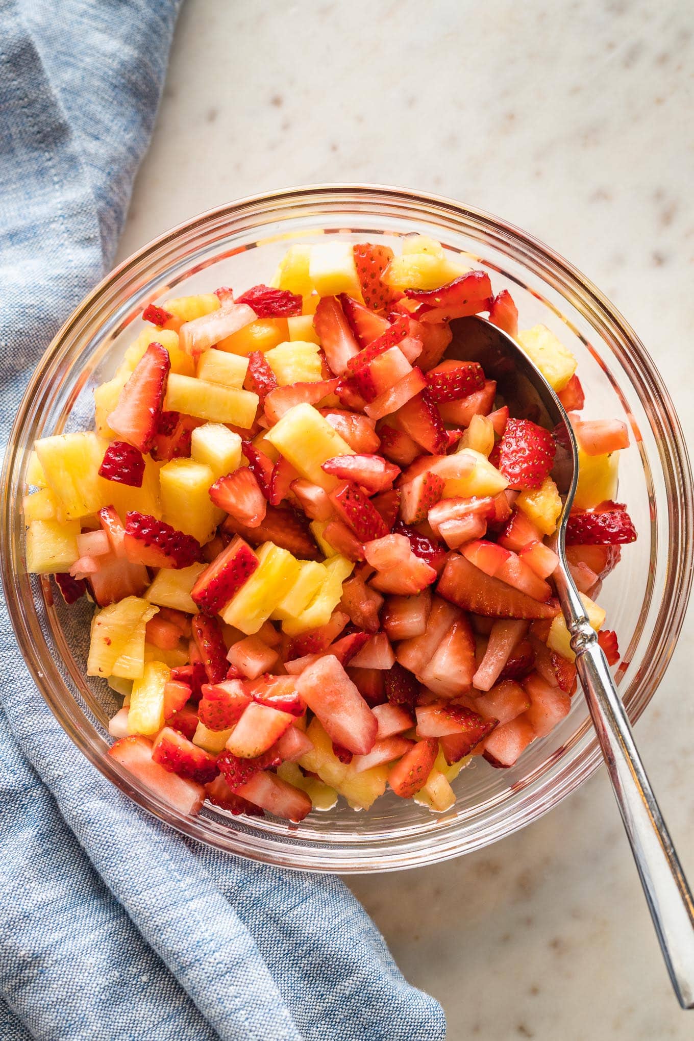 Diced strawberries and pineapple chunks mixed together in a clear glass serving bowl.
