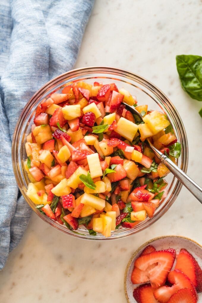 Sweet strawberry pineapple salsa with basil and balsamic vinegar served as a dip in a clear glass bowl.