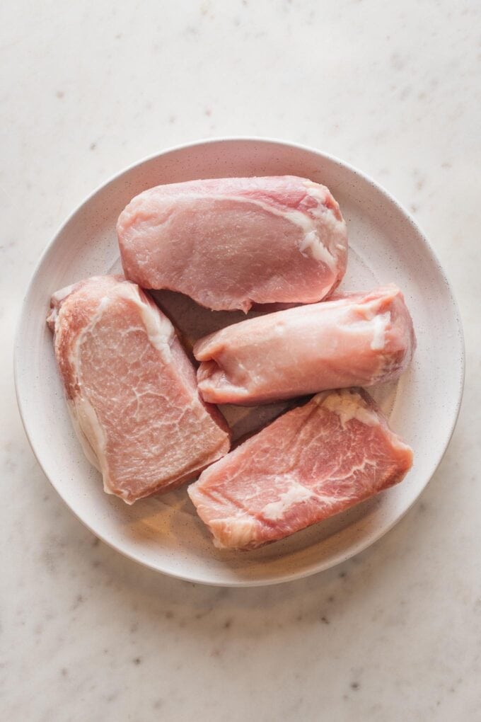 Close up of thick-cut pork chops on a plate, ready to be seasoned.