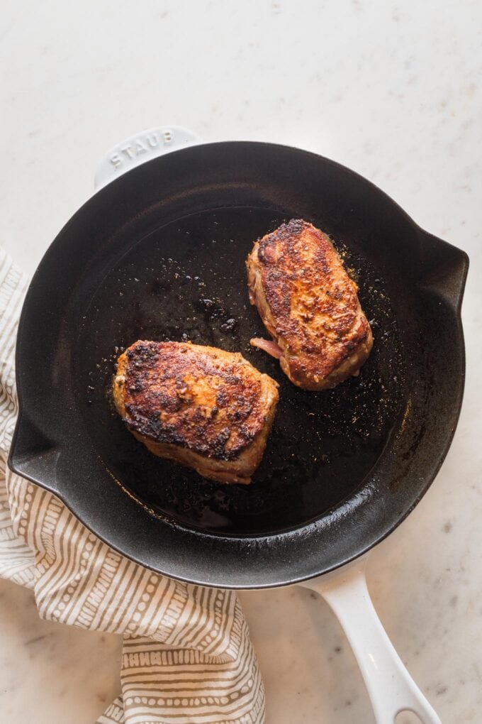 Two pork chops seared, but not cooked all the way through, in an oven-safe skillet.