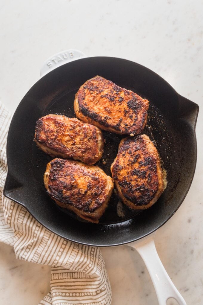 Four pork chops in a skillet, seared and ready to transfer to the oven.