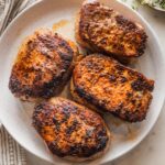 Four seared and baked boneless pork chops arranged on a white plate.