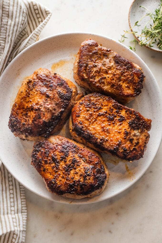 Four seared and baked boneless pork chops arranged on a white plate.