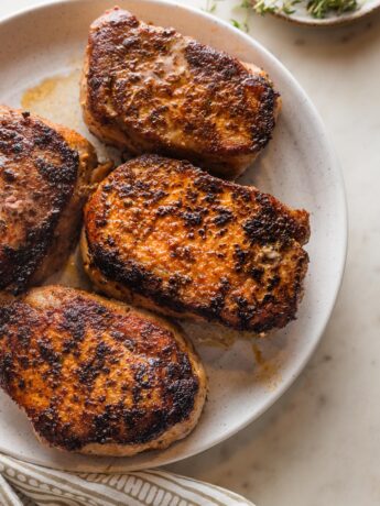 White serving plate holding four seared and baked boneless pork chops with a dark, flavorful crust.