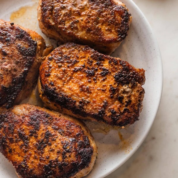 White serving plate holding four seared and baked boneless pork chops with a dark, flavorful crust.