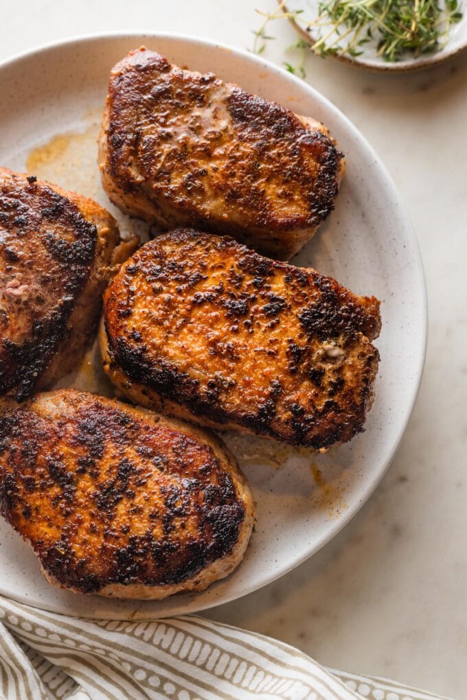 White serving plate holding four seared and baked boneless pork chops with a dark, flavorful crust.