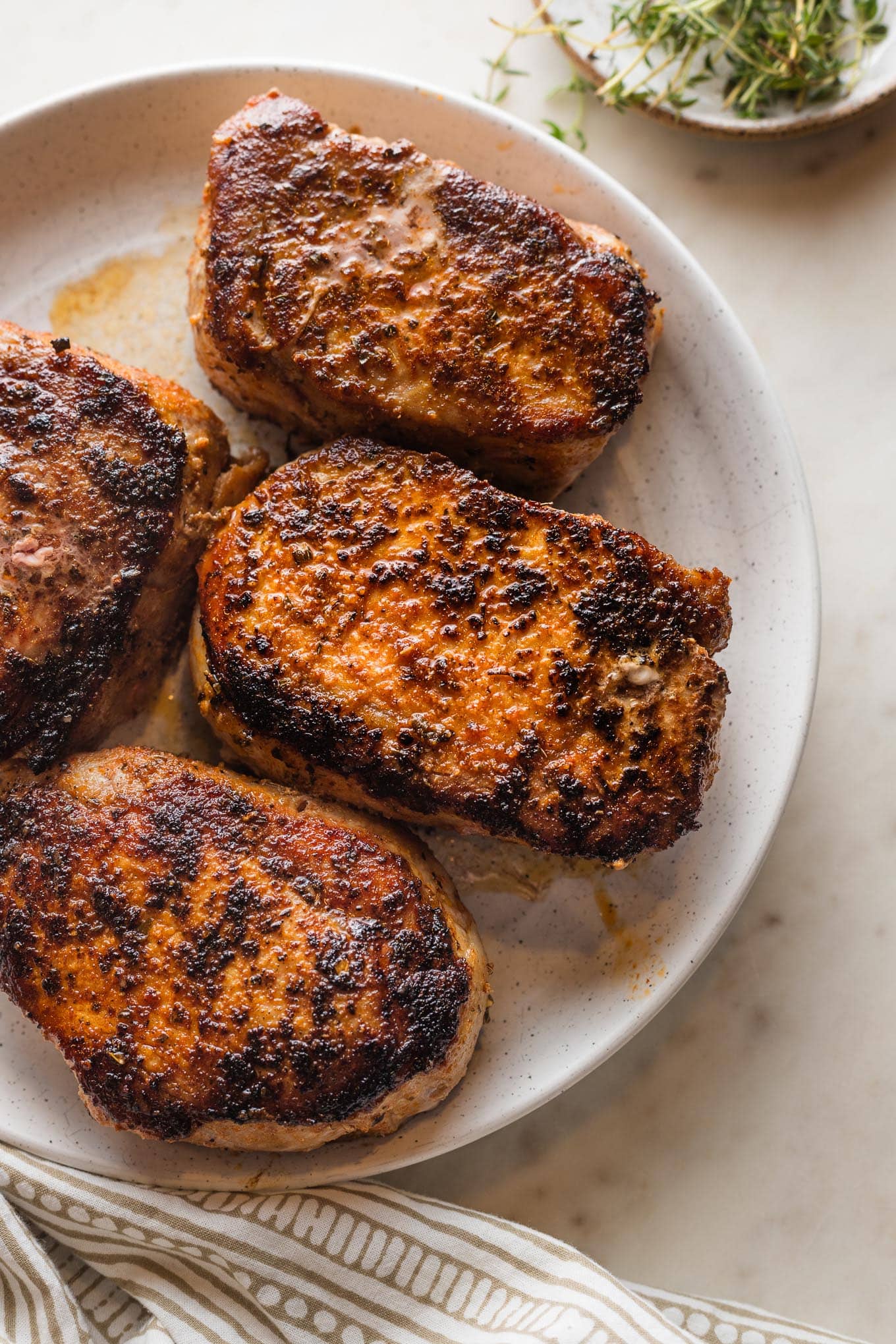 White serving plate holding four seared and baked boneless pork chops with a dark, flavorful crust.