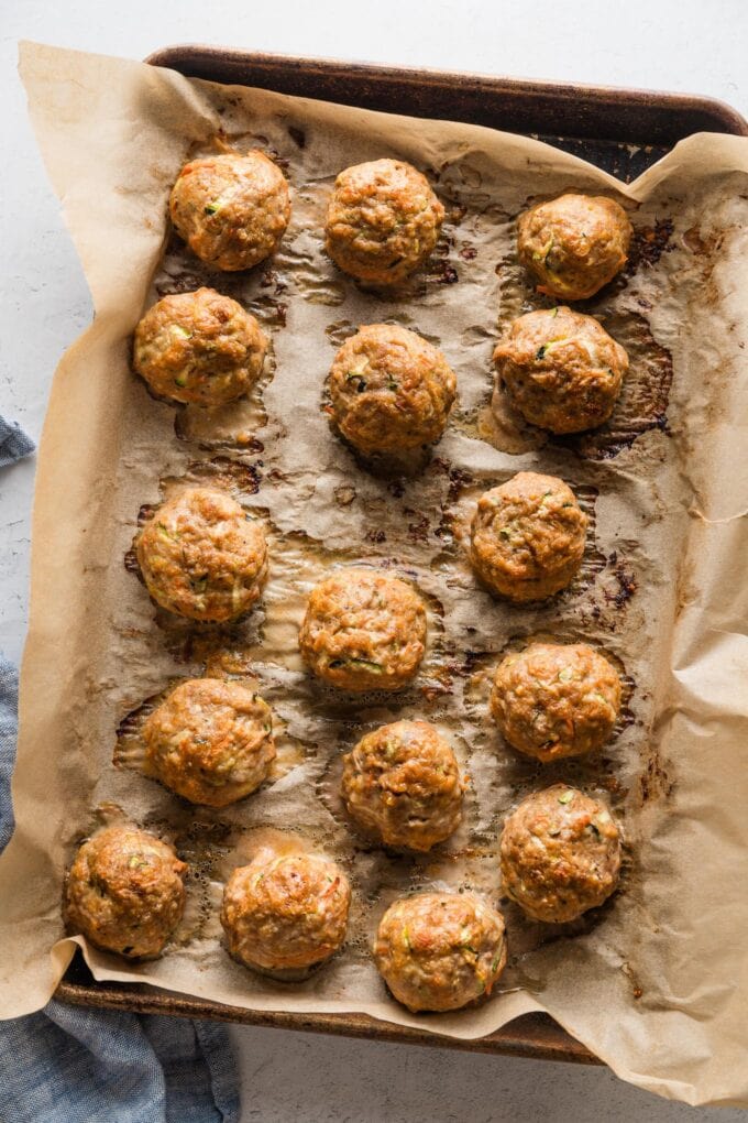 Large rimmed sheet pan lined with parchment and filled with baked turkey meatballs straight out of the oven.