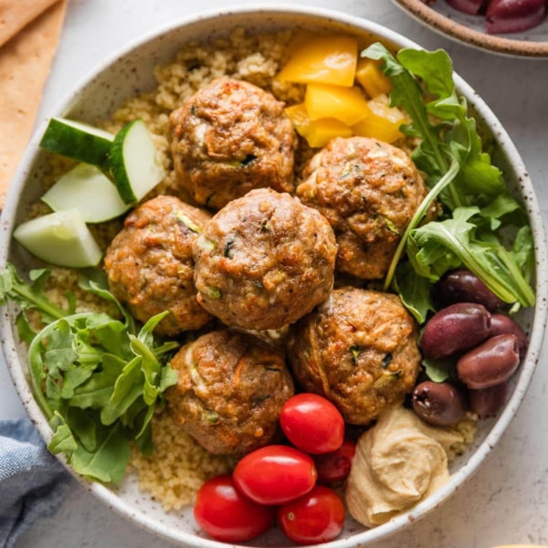 Bowl full of baked turkey meatballs served with couscous, arugula, and assorted veggies.
