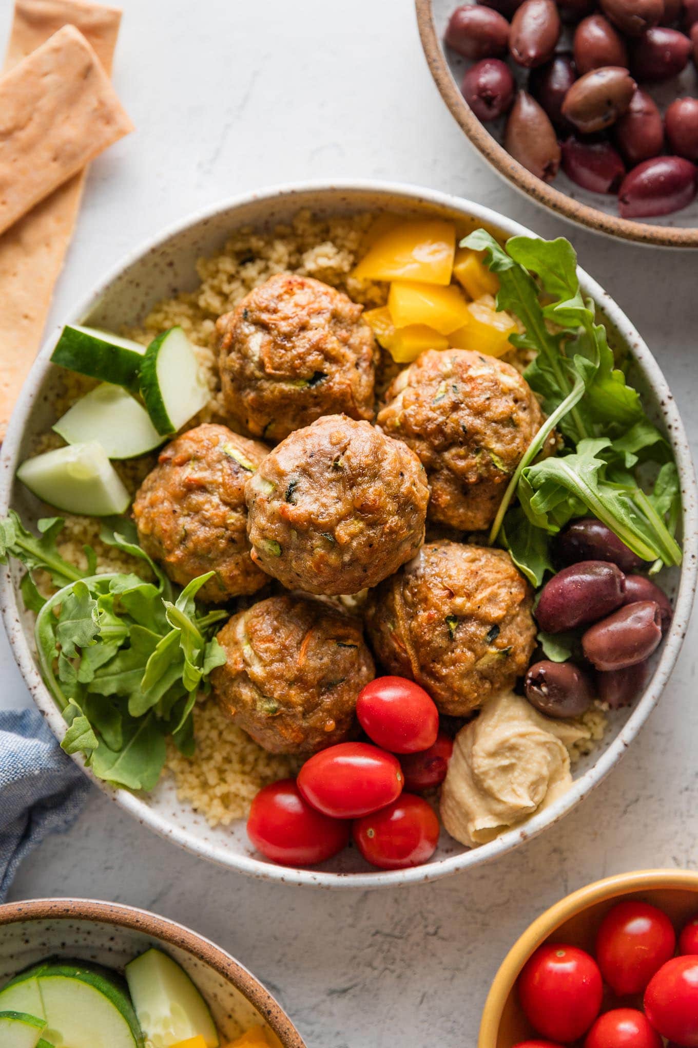 Bowl full of baked turkey meatballs served with couscous, arugula, and assorted veggies.
