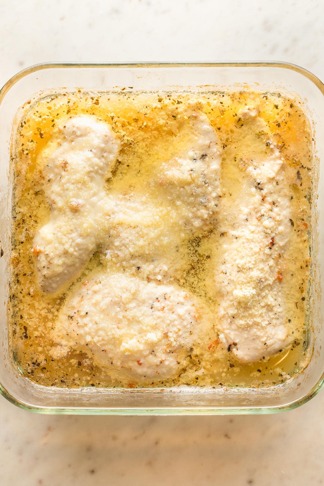 Mostly baked chicken with Parmesan cheese sprinkled on top.