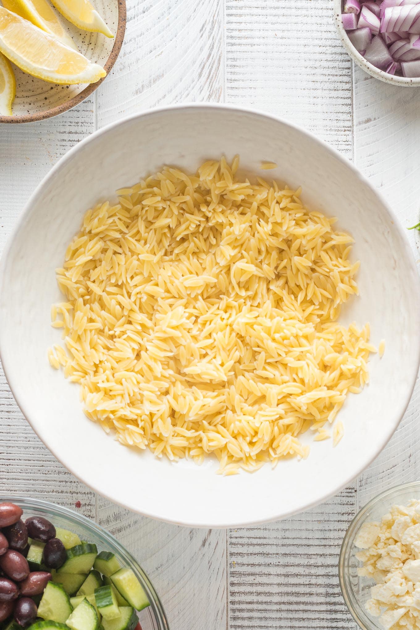 Cooked orzo slightly cooled and placed in a white serving bowl.