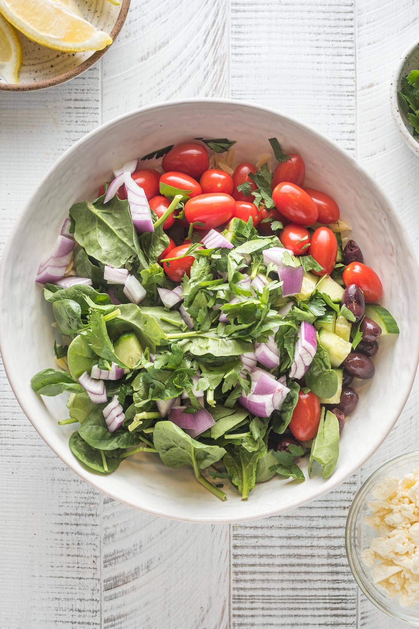 Spinach, cucumbers, onion, and cherry tomatoes added to orzo in white serving bowl.