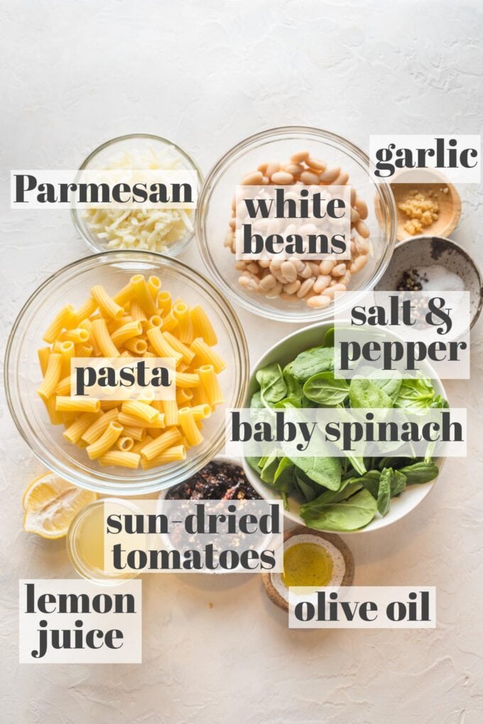 Labeled photo with prep bowls holding pasta, white beans, baby spinach, sun-dried tomatoes, olive oil, lemon juice, Parmesan, garlic, salt, and pepper.