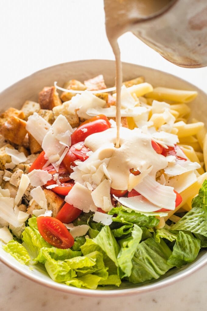Caesar dressing being poured over a pasta salad.